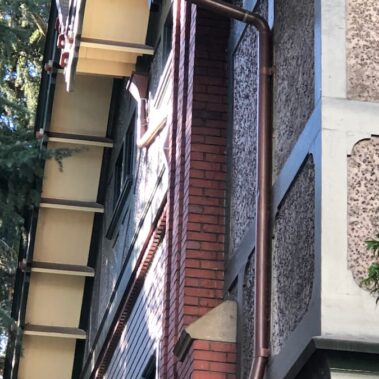 Royal Gutters' aged copper round downspout installation - classic patina finish for Portland heritage homes. Expert service: 503-558-8700