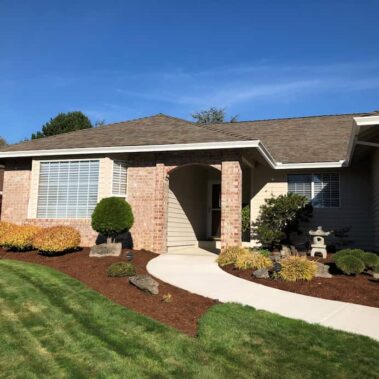 White box-bottom gutters installed on tan house with brick accents, showcasing clean lines and curb appeal with Japanese-inspired landscaping