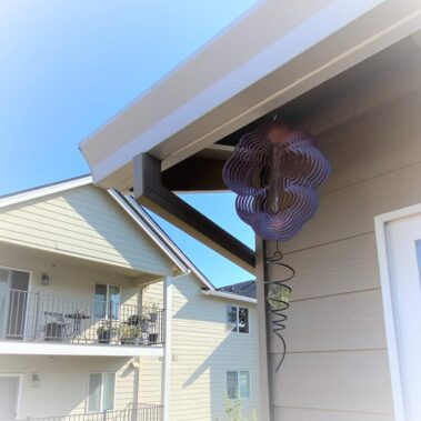 White craftsman gutter with square downspout installed on light-colored siding, featuring decorative wind spinner nearby, showcasing seamless integration