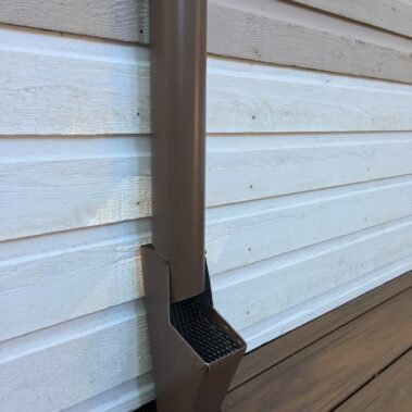 Brown round downspout cleanout installation on white lap siding, showing professional gutter maintenance access point for easy debris removal