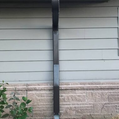 Royal Gutters brown corrugated downspout with cleanout feature, showcasing versatile installation on various siding types and compatibility with landscaping