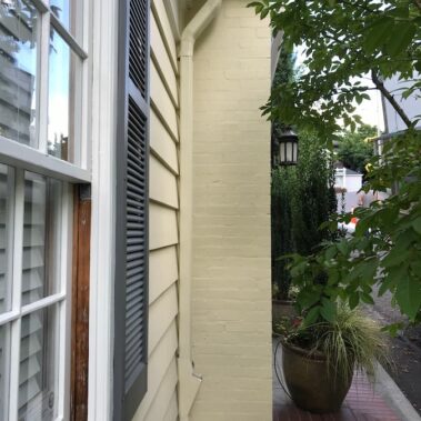 Royal Gutters seamless white gutter system on cream-colored siding, showcasing clean installation and perfect blend with lush landscaping for enhanced curb appeal