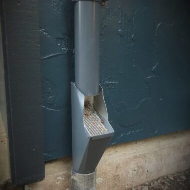 Colonial blue round downspout with built-in leaf filter cleanout system, showcasing Royal Gutters' practical maintenance solution in traditional style