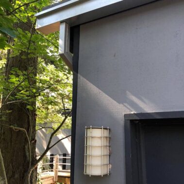 Royal Gutters Portland commercial gutter system - sleek white gutters with square downspouts on modern gray building, surrounded by lush greenery