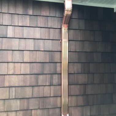 Copper 3x4 gutter system with cleanout and max flow outlet installed on dark wooden shingle house, showcasing efficient water management for Pacific Northwest homes