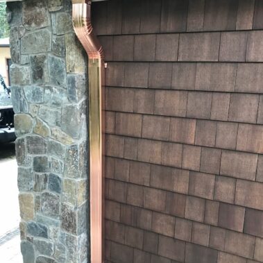 3x4 copper downspout with max flow outlet installed on stone wall and cedar shingles, showcasing premium water management for Portland homes