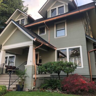 Close-up of copper metallic half-round gutter with round downspout, showing brilliant copper finish and expert craftsmanship against yellow siding