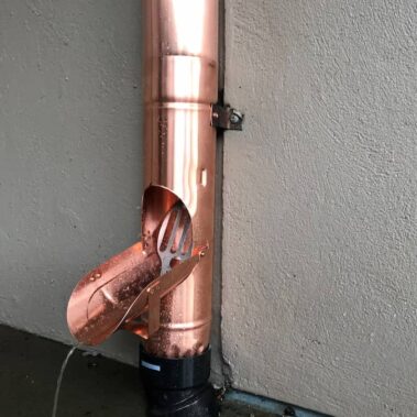 Copper round cleanout and downspout detail showing maintenance-friendly design with easy-access outlet for efficient gutter system cleaning