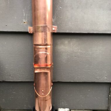 Closed copper round cleanout on downspout, showcasing seamless integration and professional installation by Royal Gutters for easy maintenance access