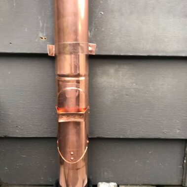 Copper round cleanout in closed position showing seamless integration with downspout, demonstrating professional finish and weather protection