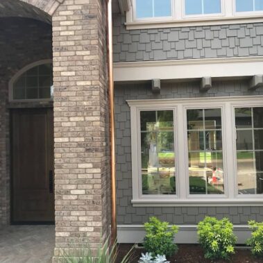 Copper round downspout installation on modern home with stone and grey shingle siding, showcasing seamless integration with mixed exterior materials