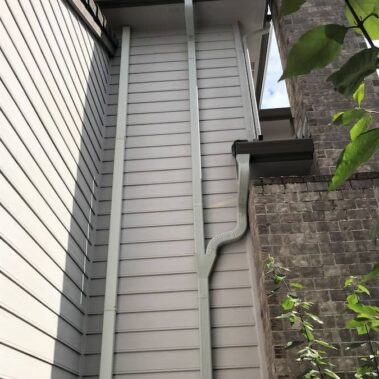 Corrugated downspout with max flow outlets and funnel system installed on siding, showcasing efficient water management for multi-story homes