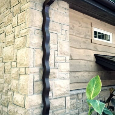 Custom wavy downspout installation by Royal Gutters Portland - designer black gutter system on stone facade, professional installation
