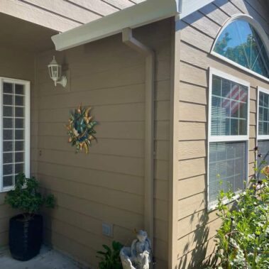 White box-bottom gutter detail showing clean installation on craftsman-style home with arched windows and beige siding, demonstrating superior soffit protection