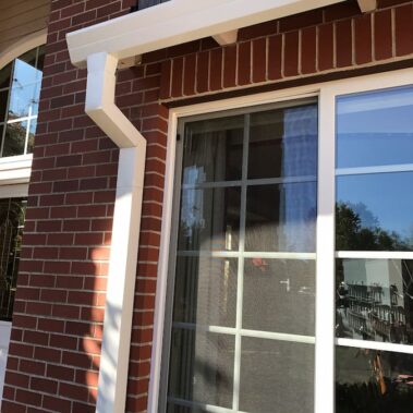 Royal Gutters' white square downspout with Max Flow outlet - professional brick facade installation, seamless fascia integration. 503-558-8700